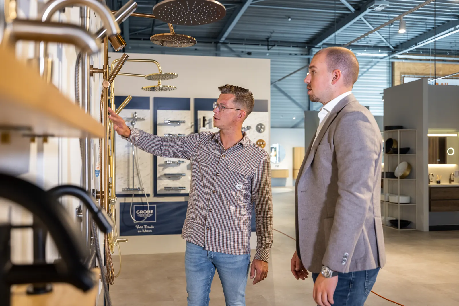 Medewerker legt een collega de kranenwand uit in de Sani4All-showroom in Harderwijk