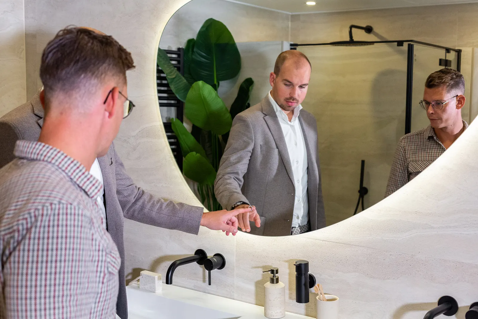 Uitleg bij een badkameropstelling met spiegel en kraan in de Sani4All-showroom in Harderwijk