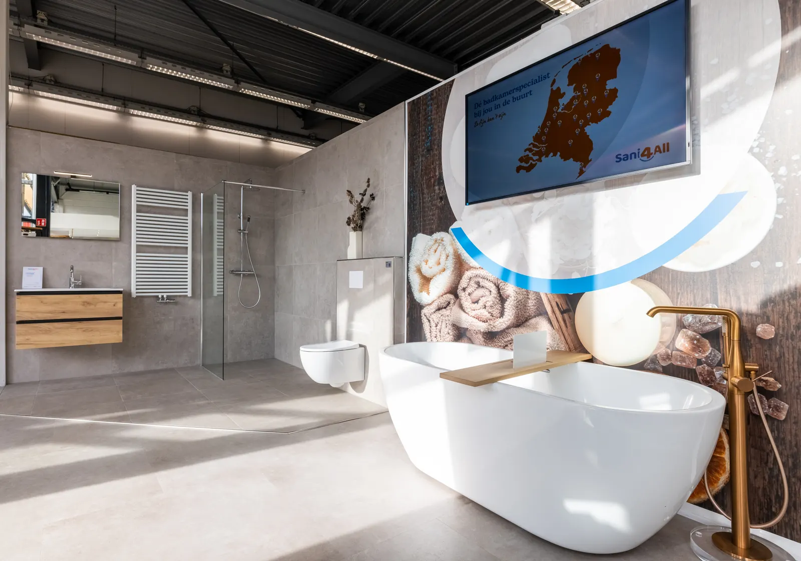 Badkameropstelling met vrijstaand bad en gouden kraan in de Sani4All-showroom in Dronten
